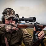 En jägare som siktar med ett Hawke Endurance 30 FD 2-12x50 kikarsikte monterat på ett jaktgevär ute i naturen.