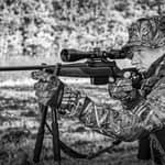 Svartvit bild på en jägare i kamouflagekläder som siktar med ett Hawke Endurance 30 FD kikarsikte monterat på ett gevär