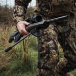 En jägare bär ett gevär utrustat med Spartan Javelin Lite benstöd monterat under pipan.