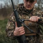 En jägare monterar ett Spartan Javelin Lite benstöd i en adapter på ett gevär ute i fält.