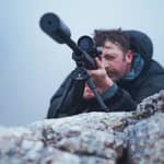 En jägare siktar med ett gevär utrustat med Spartan Javelin Lite TL benstöd monterat på en stenig bergstopp.