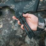En jägare håller ett hopfällt Spartan Javelin Pro Hunt Tac benstöd i kolfiber i handen utomhus.