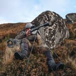 En jägare i sittande skjutställning i stenig terräng använder ett Spartan Springbok bipod monterat på ett gevär.