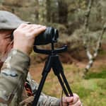 Närbild på en jägare som använder Spartan Springbok Quad som stöd för en handkikare i skogsmiljö.