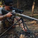En jägare som siktar med ett gevär monterat på ett Spartan Springbok kolfiberstativ ute i terrängen.