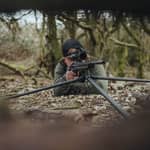 En jägare som siktar med sitt gevär monterat på ett Spartan Springbok tripodstativ i liggande position i skogen.