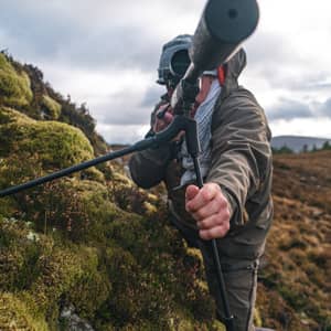 En jägare siktar med ett gevär monterat på ett Spartan Springbok bipod benstöd i en bergig terräng.