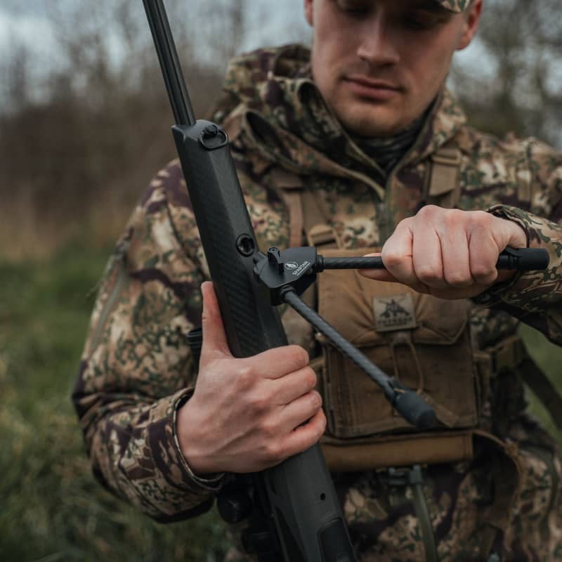 En jägare monterar ett Spartan Javelin Lite benstöd i en adapter på ett gevär ute i fält.
