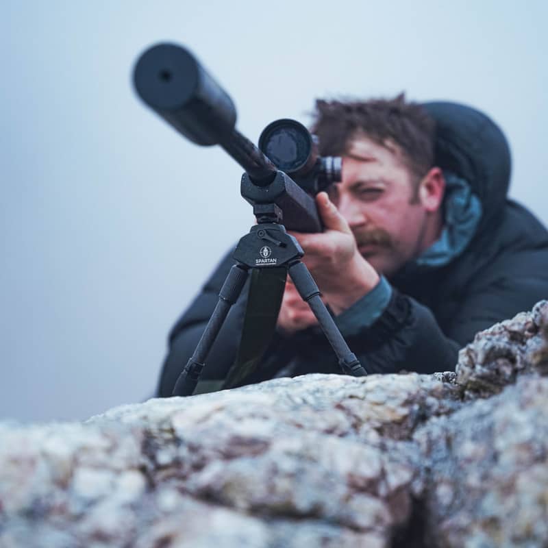 En jägare siktar med ett gevär utrustat med Spartan Javelin Lite TL benstöd monterat på en stenig bergstopp.