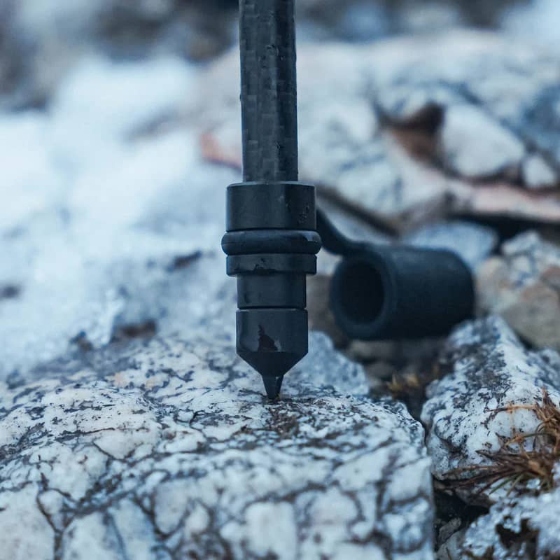 Närbild på kolfiberbenet och volframspetsen på ett Spartan Javelin Pro Hunt Tac benstöd mot en sten.