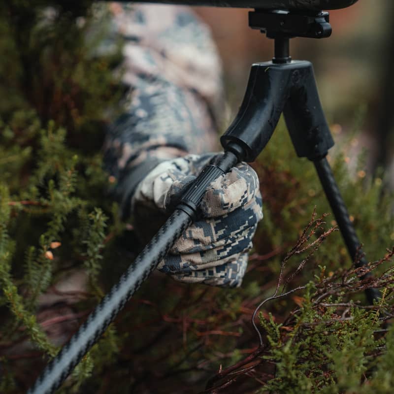 Närbild på en jägare som justerar benen på en Spartan Springbok bipod i kolfiber ute i terrängen.