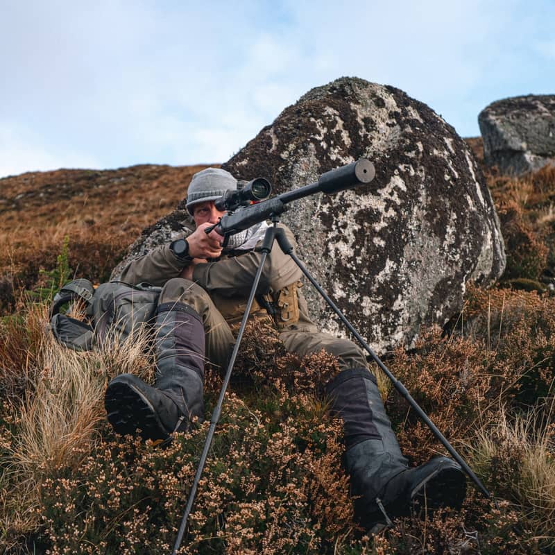 En jägare i sittande skjutställning i stenig terräng använder ett Spartan Springbok bipod monterat på ett gevär.