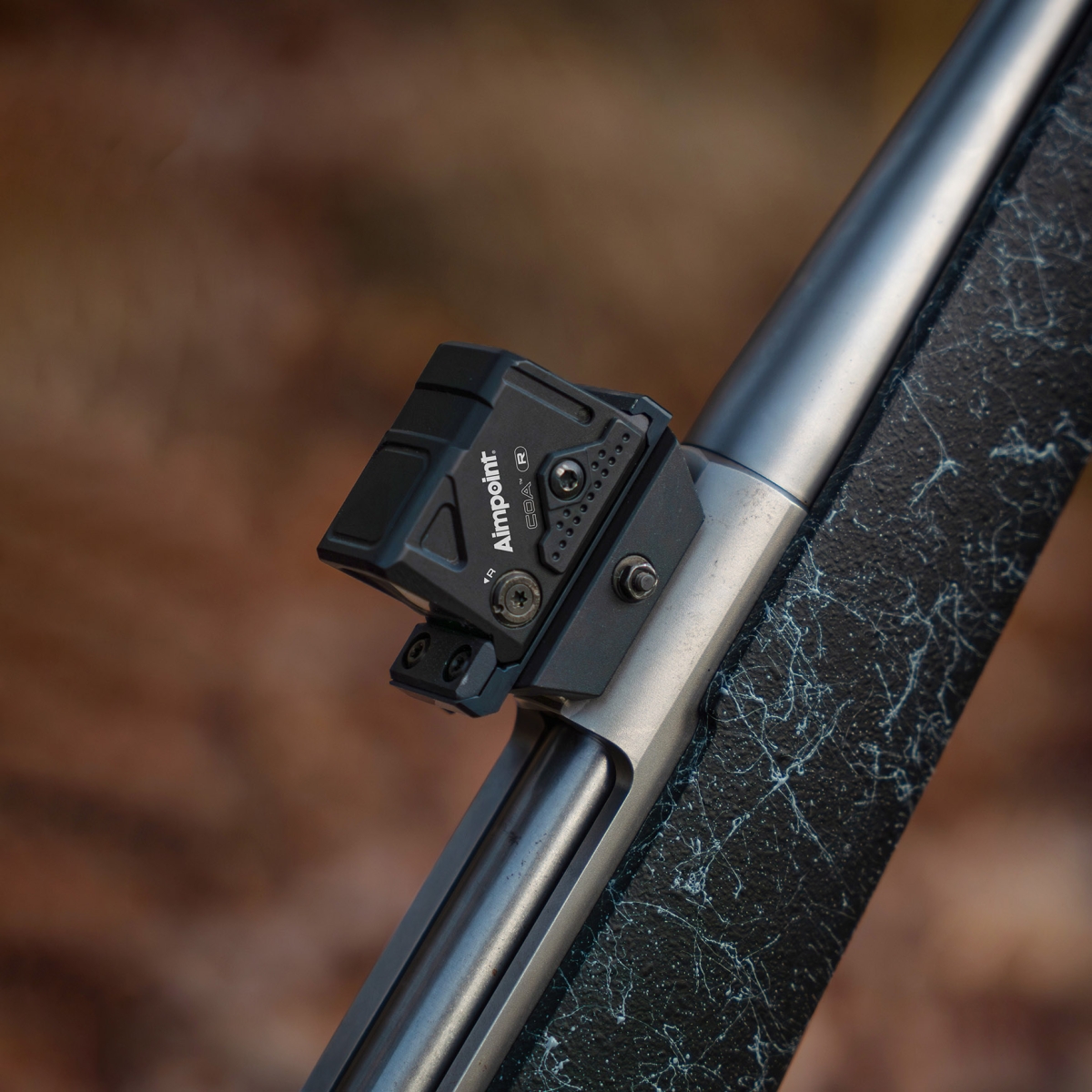 Aimpoint COA R monterad detalj Närbild på ett Aimpoint COA R rödpunktssikte monterat på ett gevär i skogsmiljö