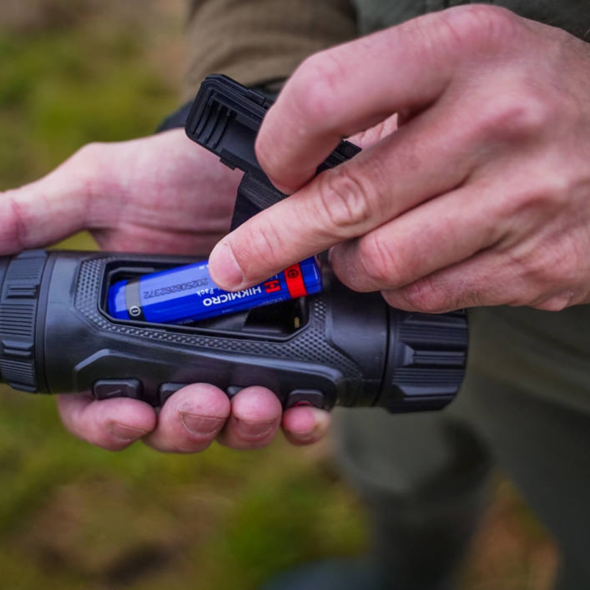 Hikmicro Lynx LQ35L 3.0 batteribyte Närbild på en person som sätter in ett blått Hikmicro-batteri i batterifacket på en Hikmicro Lynx LQ35L 3.0 termisk monokulär.