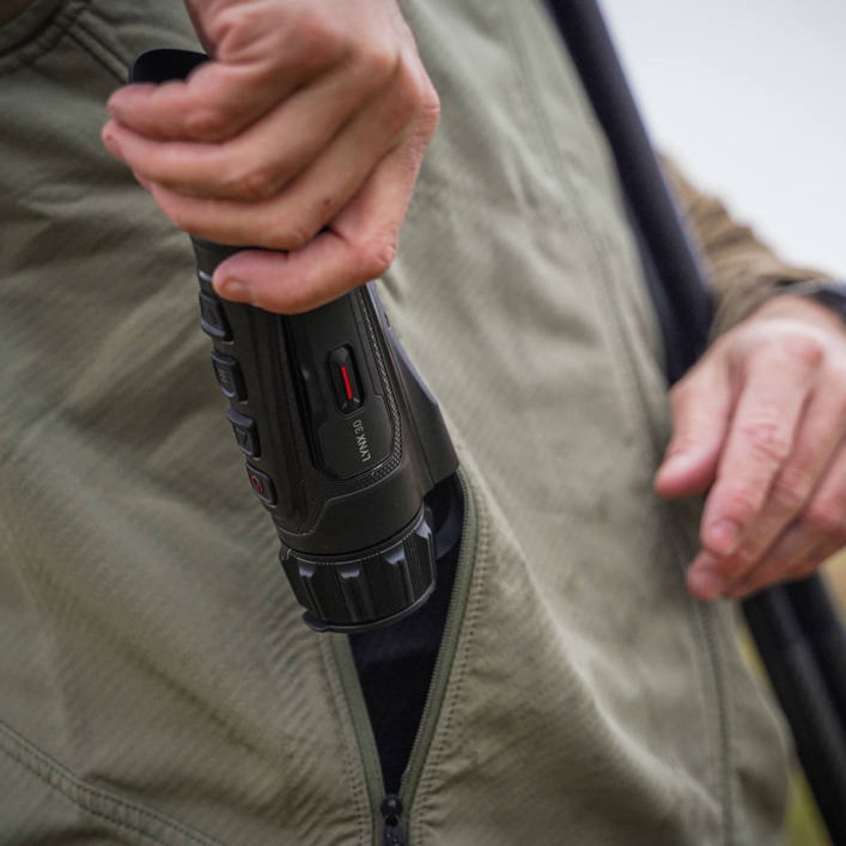 Hikmicro Lynx LQ35L 3.0 i ficka Närbild på en person som stoppar ner en Hikmicro Lynx LQ35L 3.0 termisk monokulär i en grön jackficka.